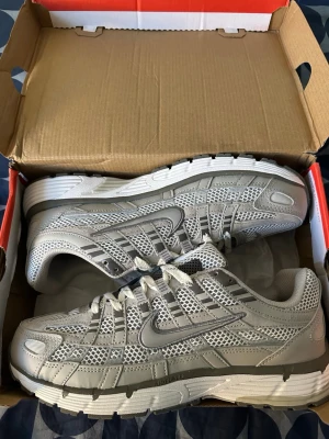 Nike grå p6000 - Snygga grå sneakers från Nike med meshpaneler och detaljer i syntetmaterial. Skorna har en sportig vibe med tydlig swoosh-logga på sidan och robust sula. Perfekta för dig som gillar streetwear och vill ha en clean look.