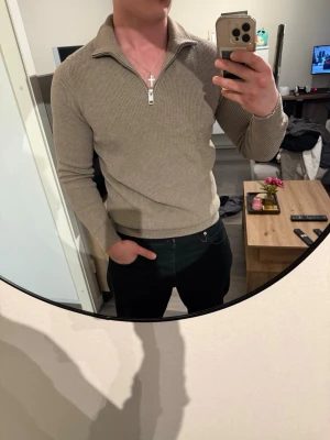 Beige stickad tröja med dragkedja - Säljer en beige stickad tröja från H&M med halv dragkedja och krage. Tröjan har lång ärm och är ribbstickad vilket ger en snygg och stilren look. Perfekt för lager på lager och enkel att matcha med olika outfits.