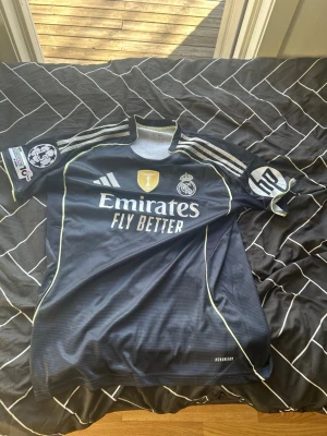 Real Madrid Mbappé #10 matchtröja – NY – Storlek M Slim Fit – Alla detaljer - Säljer en riktigt snygg och helt ny Real Madrid-tröja med Mbappé #10. Tröjan är aldrig använd, endast testad – prislappen är borttagen men skicket är 100% nyskick.   Detta är en modell med alla detaljer: Champions League-märke på ärmen, sponsortryck, klubbmärke och högkvalitativt material (AEROREADY). Perfekt för dig som vill ha en exklusiv matchtröja som sticker ut.  • Storlek: M (Slim Fit – sitter tajt och sportigt) • Skick: Helt ny • Spelare: Mbappé #10 • Alla patches och detaljer på plats 