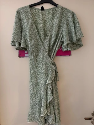 Grön blommig omlottklänning med volang - En blommig omlottklänning från SHEIN i tunt material och skön på sommaren. Står att det är m men skulle säga mer xs/s