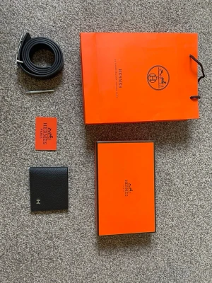 Svart H bälte och plånbok  - Snygg svart plånbok från H i exklusivt läder med diskret logga framtill. Plånboken har flera kortfack och ett fönster för ID-kort. Perfekt för dig som vill ha en stilren och lyxig accessoar i vardagen.