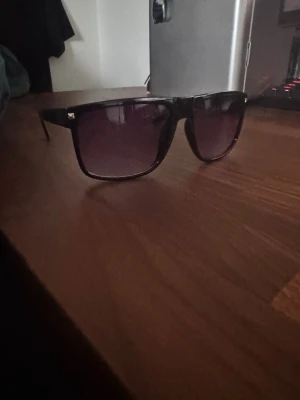 Tonade glasögon - Snygga solglasögon med svart båge. Glasen är mörka och ger en cool look, perfekt för soliga dagar. Klassisk design som passar till det mesta och ger en trendig vibe. Liknar kända raband boyfriend modellen, helt nya
