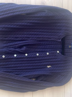 Marinblå kofta Polo Ralph Lauren - Säljer en marin blå kofta från Polo Ralph Lauren med rund halsringning och vita knappar framtill. Ska passa till en som är 16, skulle säga att storleken är xxs-xs
