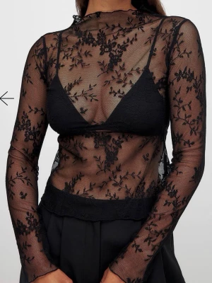 Svart spetsblus från NA-KD - Transparent svart blus från NA-KD i mesh med blommigt spetsmönster. Hög hals och långa ärmar. Perfekt att styla lager på lager eller med en snygg topp under. Tunn och lätt, ger en trendig och edgy look. Nypris 300