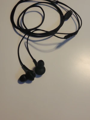Svarta in-ear hörlurar från Samsung  - Säljer ett par svarta in-ear hörlurar från Samsung med sladd och silikonproppar. Hörlurarna har en stilren design och platt kabel som minskar trassel. Perfekta för musik, poddar eller samtal på språng.Har använts nån gång men har tappat bort kartongen som den kom i. Funkar till alla telefoner som har USB-C laddport. Nypris 200kr