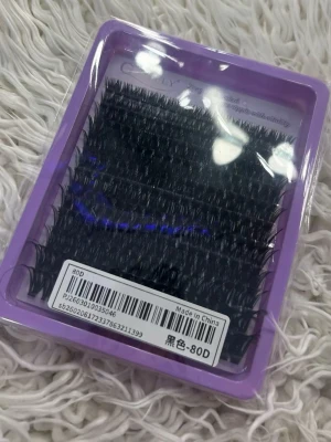 Svarta volymfransar 80D i ask - Ett paket svarta volymfransar i 80D, perfekta för att skapa fylliga och dramatiska ögonfransar. Fransarna kommer i en lila ask och är gjorda av syntetmaterial. Passar för dig som vill ha en intensiv look till ögonen.