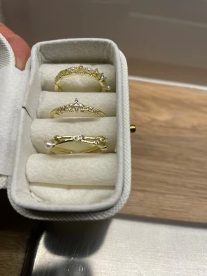 3 rostfria & justerbara ringar - Säljer ett set med tre guldfärgade ringar med gnistrande stenar och dekorativa detaljer. En av ringarna har en liten pärla och de andra har vackra mönster med små stenar. Perfekt för dig som gillar stilrena och trendiga accessoarer. Rostfritt material ( Copper), alla är justerbara o storleken. Skickas med en fin guldig ask ( sista bilden)🌸
