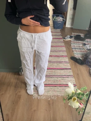 Vita linnebyxor med rak passform - Säljer ett par vita linnebyxor med avslappnad rak passform och resår i midjan. Byxorna är tunna och luftiga, perfekta för varma dagar. Inga synliga fickor eller detaljer. Passar dig som gillar en enkel och clean stil.