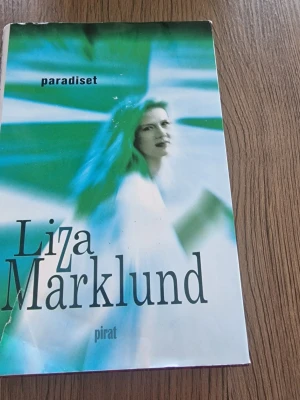 Paradiset av Liza Marklund - Säljer boken 'Paradiset' av Liza Marklund, utgiven av Piratförlaget. Omslaget har en blågrön abstrakt design med svart text. Romanen är en del av serien om journalisten Annika Bengtzon och bjuder på spänning och drama.