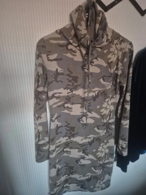 Camouflageklänning med organised army-look - Cool långärmad klänning från Gina Tricot i camouflage-mönster. Klänningen har hög krage med snörning och är tillverkad i mjuk bomullsmix. Perfekt för dig som vill sticka ut med en streetstyle-vibe.