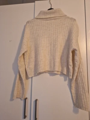 Beige ribbstickad croppad polotröja - Säljer en beige ribbstickad croppad polotröja med långa ärmar och hög krage. Tröjan har en avslappnad passform och är perfekt för lager-på-lager. 