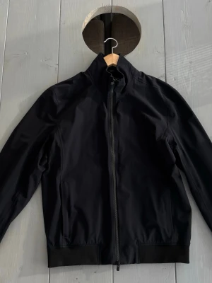 Svart vindjacka med dragkedja - Säljer en stilren svart jacka från UBR. Jackan är i mycket fint skick och har en modern, minimalistisk design som passar både till vardag och mer uppklädda tillfällen. Den är lätt, bekväm och perfekt för vår, höst eller svala sommarkvällar. Hög krage, dragkedja framtill och praktiska fickor. UBR är känt för sin höga kvalitet och funktionella plagg. En tidlös jacka som är enkel att matcha med resten av garderoben. Hör av dig vid intresse eller frågor!