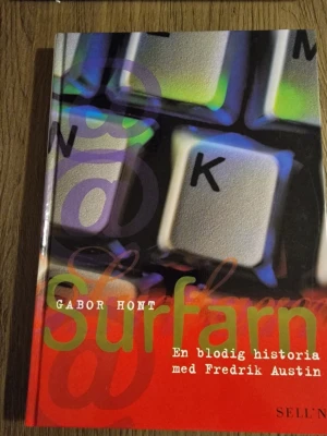 Surfarn: En blodig historia - En spännande roman av Gabor Hont och Fredrik Austin som utforskar identitet, blodtransfusioner och teknik. Omslaget har ett färgstarkt tryck med tangentbord och röda, gröna och lila toner. Perfekt för dig som gillar samtida och tankeväckande skönlitteratur.