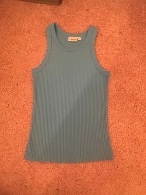 Blå ribbad linnetopp från Kappahl - Snygg blå ribbad linnetopp från Kappahl. Toppen är ärmlös med rund halsringning och har en tight passform. Perfekt att matcha med jeans eller kjol för en fräsch look.