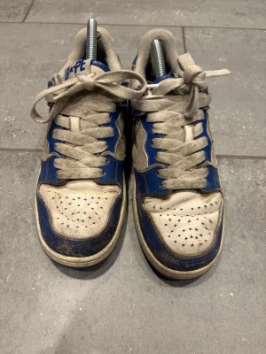 Blå och vita BAPE STA sneakers - Säljer ett par klassiska BAPE STA sneakers i blått och vitt med den ikoniska stjärndesignen på sidan. Skorna har snörning och är tillverkade i skinn med detaljer i syntet. Perfekta för dig som vill sticka ut med streetwear-vibe.