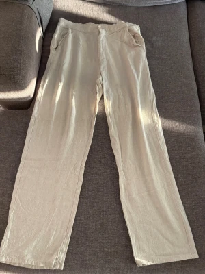 Beiga linnebyxor från Grunt - Snygga beiga linnebyxor från Grunt med avslappnad passform och raka ben. Byxorna har resår i midjan och sidfickor, vilket gör dem både bekväma och stilrena. Perfekta för en chill och trendig look under varmare dagar.