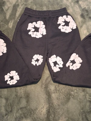 Svarta ‘cloud print’ mjukisbyxor - Säljer ett par svarta mjukisbyxor med unika vita molnliknande tryck över soppen och benen. Byxorna har resår i midjan och är gjorda i ett mjukt, bekvämt material. Perfekta för en chill och trendig look.