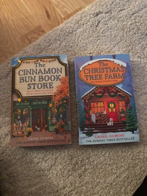 The + Christmas Tree Farm & Cinnamon Bun Book Store - Två engelskspråkiga pocketböcker av Laurie Gilmore: 'The Cinnamon Bun Book Store' med hö basfärger och bokhandel på omslaget, samt 'The Christmas Tree Farm' med vintertema och dekorerad stuga. Perfekta feelgood-romaner för dig som gillar mysiga berättelser.