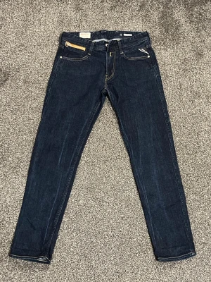Replay Anbass jeans – W29 L30 – mörkblå – nyskick - Säljer ett par Replay Anbass jeans i storlek W29 L30. Väldigt fint skick.  Snygga mörkblå jeans med smal passform och en cool guldfärgad dragkedja på fickan. Klassiska bakfickor med kontrastsömmar och läderpatch i midjan. Jeansen har också en snygg mörk tvätt med naturliga streck som ger en stilren look.  Behöver bara strykas lite så är de som nya.  Perfekta för dig som gillar stilrena och trendiga jeans.  Skriv om du vill ha fler bilder eller mått.