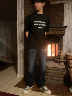 Svart Acne Studios t-shirt Stockholm - Svart t-shirt från Acne Studios med vit text 'Acne Studios STOCKHOLM 1996' på bröstet. Klassisk passform med rund hals och korta ärmar. Perfekt för dig som gillar stilrena och trendiga plagg från populära märken.