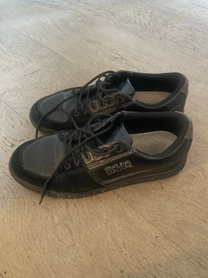 Svarta Versace Jeans Couture sneakers - Snygga svarta sneakers från Versace Jeans Couture med läder- och mockadetaljer. Skorna har klassisk låg profil, perforerad tå och tydlig logga på sidan och sulan. Perfekta för dig som vill ha en stilren och exklusiv look.