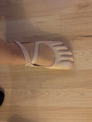 Vibram FiveFingers sandaler baby pink/orange - Unika tå-sandaler från Vibram i baby pink med orange sula och detaljer. Modellen har separata fack för tårna, justerbar rem över foten och greppvänlig sula. Perfekta för dig som gillar barfotakänsla och vill ha något annorlunda till sommaren.