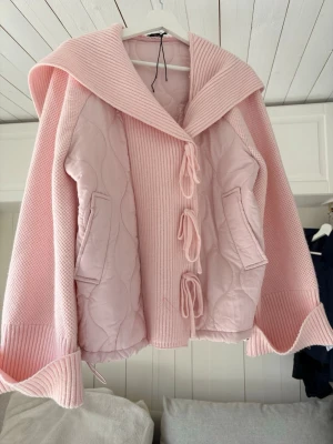 Rosa quiltad cardigan jacka med knyt - Supersöt rosa cardigan jacka med quiltade partier och bred krage. Jackan har knytstängning framtill, två fickor och ribbade muddar. Perfekt för dig som vill ha en mysig och trendig look med oversized känsla. Pris går att diskutera!