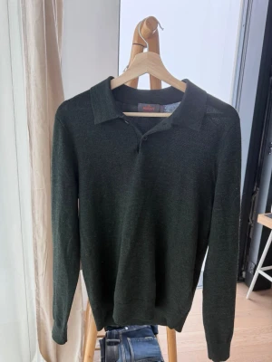 Mörkgrön stickad tröja med krage - Snygg mörkgrön stickad tröja från Morris med klassisk krage och knäppning vid halsen. Långärmad modell i tunt, mjukt material som passar perfekt till jeans eller chinos. Enkel och stilren design för en avslappnad look. 100% merinoull