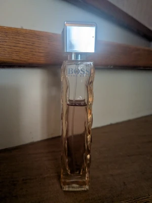 BOSS parfym med vågig flaska - Elegant parfym från BOSS i en genomskinlig, vågformad glasflaska med ljusbrun ton och en stilren, silverfärgad fyrkantig kork. Perfekt för dig som gillar klassisk och modern design.  Mängd enligt bild 