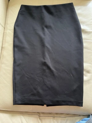 Svart pennkjol i bomull - En klassisk svart pennkjol i mjukt bomullsmaterial. Kjolen har en rak och tight passform som slutar strax ovanför knät. Perfekt att styla med en crop top eller oversized tröja för en clean look.