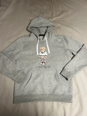 Grå Polo Bear Ralph Lauren hoodie - Säljer en helt sprillans ny polo bear Ralph Lauren hoodie. Storlek L men passar bättre på M. Skriv vid minsta fundering.