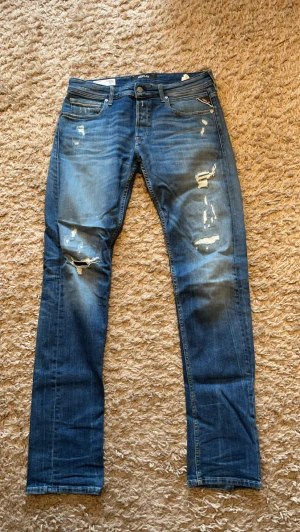 Blå  jeans från Replay - Säljer ett par blå jeans från Replay med slitningar och hål på knäna för en cool, avslappnad look. Replay grover storlek 31/34