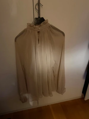Beige chiffongblus med volangkrage - Ida Sjöstedt blus, super fin med pärl detaljer på backe och båda handlederna. Använd 1-2 gånger bara då den tyvärr inte passar, strl 38 