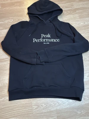 Svart hoodie Peak Performance - Svart hoodie från Peak Performance med broderad vit logga i storlek L.