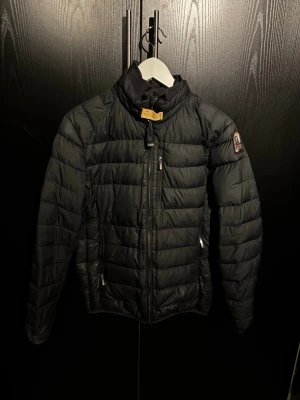 Svart dunjacka från Parajumpers - Svart dunjacka från Parajumpers med quiltad design och hög krage. Jackan har dragkedja framtill, två sidofickor med dragkedja och ett snyggt PJS-märke på vänster ärm. Perfekt för lite kyligare dagar och riktigt stilren.