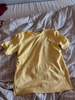 Gul basic t-shirt i bomull - En enkel och stilren gul t-shirt i mjuk bomull. T-shirten har rund halsringning och korta ärmar, perfekt för en avslappnad look. Passformen är normal och tyget känns skönt mot huden. 