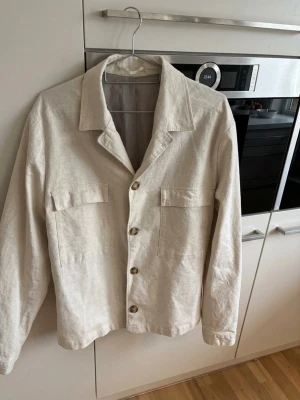 Beige linnekavaj - Stilren beige overshirt i ett lätt linneliknande material. Klassisk krage, fyra knappar framtill och två stora bröstfickor med lock. jag vill dock nämna att det finns en mindre fläck i armhålan som verkligen inte syns när jackan sitter på! gör gärna av er vid frågor!💗