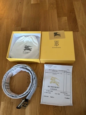 Svart Burberry bälte med rutigt mönster - Snyggt svart bälte från Burberry med klassiskt rutigt mönster och en stilren metallspänne med Burberrys ikoniska logotyp. Bältet kommer i originalförpackning med dustbag och kvitto. Perfekt accessoar för att lyfta din outfit.
