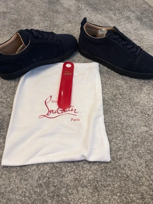 Mörkblå Christian Louboutin sneakers - Snygga mörkblå sneakers från Christian Louboutin i mocka med klassisk röd sula. Skorna har lågt skaft, svarta skosnören och diskret logga på sidan. Kommer med originalpåse och skohorn. Perfekta för dig som vill sticka ut med exklusiva detaljer. Du får endast skorna med