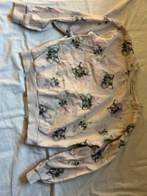 Ljus rosa sweatshirt med kattmotiv Kappahl för barn  - Supersöt ljusrosa  sweatshirt från Kappahl med tryck av kattansikten över hela tröjan. Mjuka muddar vid ärmslut och nederkant. Perfekt för dig som gillar gulliga och lekfulla prints. Tillverkad i mjukt bomullsmaterial.
