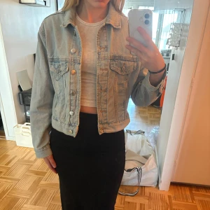 Ljusblå croppad jeansjacka från Gina tricot - Säljer en ljusblå croppad jeansjacka från Gina tricot. Jackan har klassisk krage, knappar framtill och två bröstfickor med lock. 