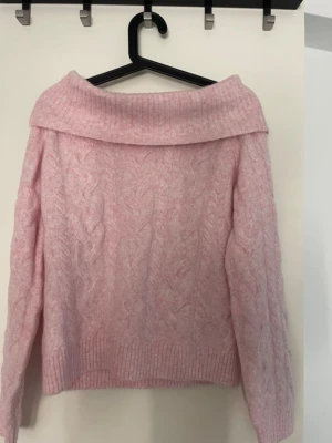 Ljusrosa kabelstickad tröja - Mysig ljusrosa stickad tröja med bred polokrage och kabelstickat mönster. Tröjan har långa ärmar och ribbade muddar vid ärmslut och nederkant. Perfekt för kalla dagar när du vill vara både varm och snygg.