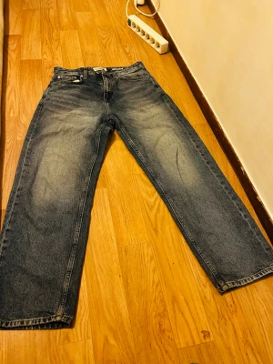 Blå relaxed dad jeans Pull&Bear - Säljer ett par blå relaxed dad jeans från Pull&Bear. De har en avslappnad passform med raka ben och klassisk femficksdesign. Jeansen är tillverkade i denim och har snygga slitningar och tvättade detaljer för en cool vintage-look. Hade lite repor på baksidan som är reparerad men den sysns ändå.  