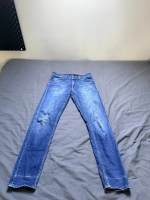 Blå slim fit jeans med slitningar - Snygga blå slim fit tiger of Sweden  jeans med lätt slitna detaljer på benen och klassisk femficksdesign. Jeansen har normal midja och raka ben. Perfekta för en avslappnad och trendig look.