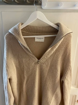 Beige stickad tröja med dragkedja - Snygg beige stickad tröja från These Glory Days med halv dragkedja och bred krage. Tröjan har ribbstickad struktur och är perfekt för lager-på-lager. Enkel och stilren design som passar till mycket.