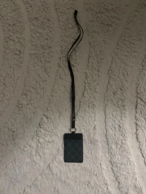  svart korthållare med band - Snyggt svart kortfodral med  långt svart band att hänga runt halsen. Perfekt för kort eller ID, tillverkat i läder med stilren design och diskreta detaljer.