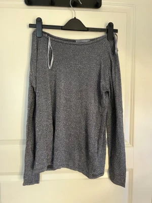 Grå glittrig långärmad topp - Snygg grå långärmad topp med glittrigt material och en avslappnad passform. Toppen har en bred halsringning . Perfekt för dig som gillar att sticka ut lite extra.