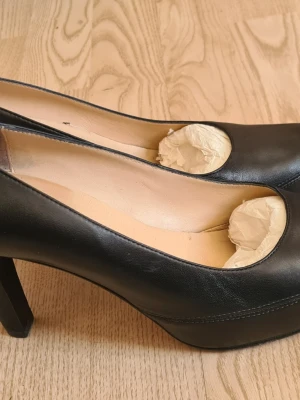 Svarta pumps från Unisa i skinn - Klassiska svarta pumps från Unisa i äkta skinn med rundad tå och hög klack. Insidan är beige och har en mjuk innersula för extra komfort. Perfekta för dig som gillar stilrena och tidlösa skor.