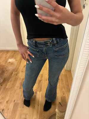 Blå bootcut jeans med fickor - Säljer ett par blå bootcut jeans med stora framfickor och dubbla knappar i midjan. Jeansen har en klassisk tvätt och markerade sömmar som ger en retrovibe. Från lager 157 i storlek 150cm. Använda ett fåtal gånger därav mycket bra skick. 