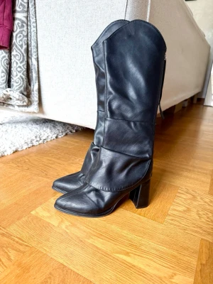 Svarta höga boots med klack - Säljer ett par svarta höga boots i mjukt skinnliknande material. Stövlarna har spetsig tå, bred klack och en cool, slouchy passform. Använda 1 gång. 